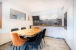 This modern kitchen and dining area boasts sleek white cabinetry, a stylish black range hood, and a beautiful wooden dining table.