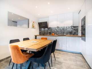 This modern kitchen and dining area boasts sleek white cabinetry, a stylish black range hood, and a beautiful wooden dining table.