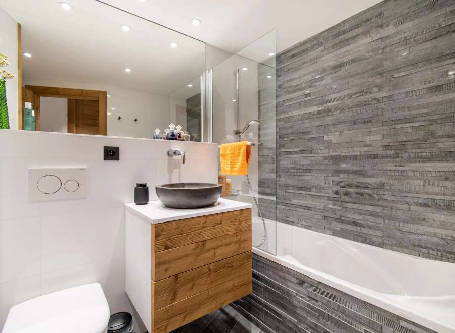 This modern bathroom features a stylish design with a wooden vanity and a sleek, stone-like accent wall.