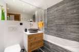 This modern bathroom features a stylish design with a wooden vanity and a sleek, stone-like accent wall.