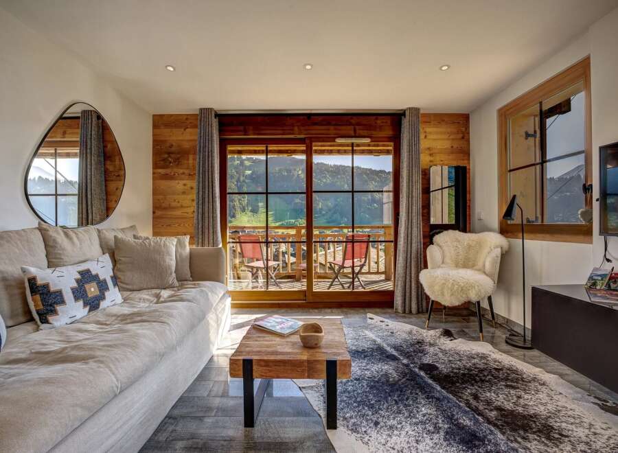 Experience breathtaking mountain views from this stunning living room, featuring a plush sofa, a rustic wooden coffee table, and a cozy sheepskin accent chair.