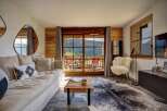 Experience breathtaking mountain views from this stunning living room, featuring a plush sofa, a rustic wooden coffee table, and a cozy sheepskin accent chair.