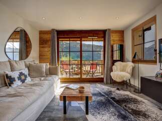 Experience breathtaking mountain views from this stunning living room, featuring a plush sofa, a rustic wooden coffee table, and a cozy sheepskin accent chair.