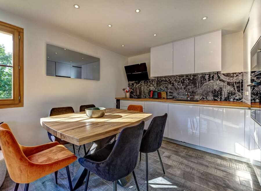This modern dining area and kitchen features a rustic wooden dining table with plush velvet chairs, perfect for intimate gatherings.