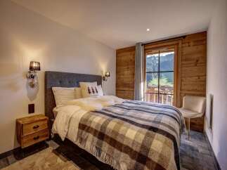 Experience cozy mountain living in this charming bedroom, featuring a plush bed adorned with a warm plaid blanket and soft pillows.