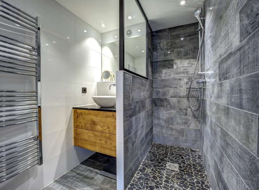 Experience modern luxury in this stunning bathroom featuring a sleek wooden vanity with a vessel sink and a spacious walk-in shower with textured grey tilework.
