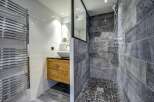 Experience modern luxury in this stunning bathroom featuring a sleek wooden vanity with a vessel sink and a spacious walk-in shower with textured grey tilework.