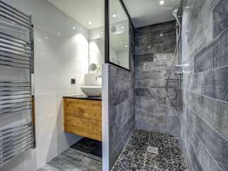 Experience modern luxury in this stunning bathroom featuring a sleek wooden vanity with a vessel sink and a spacious walk-in shower with textured grey tilework.