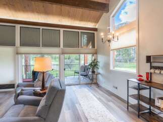 Step into this stunning living space, featuring a vaulted ceiling with exposed wooden beams and expansive windows that flood the room with natural light.