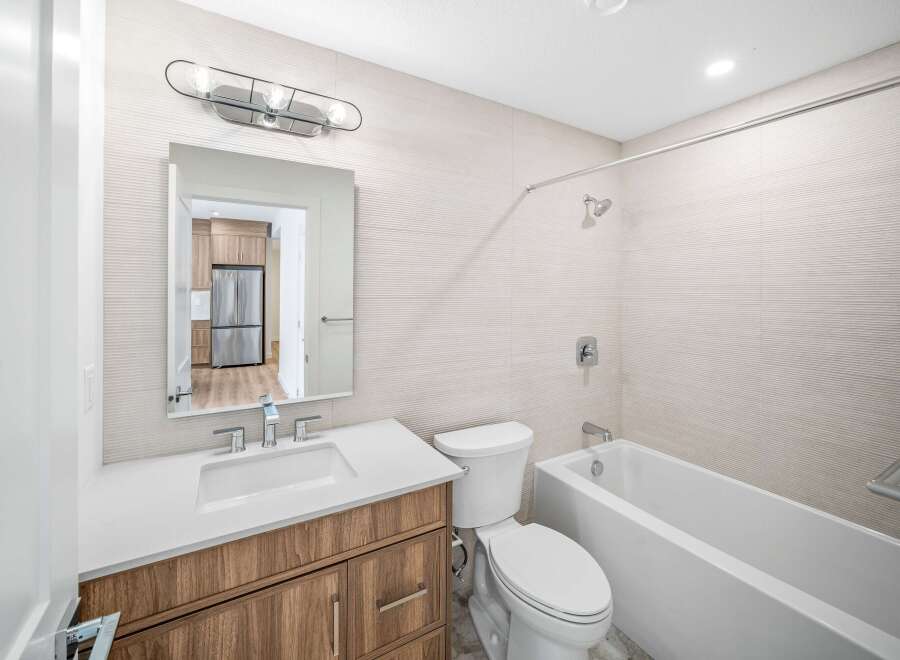 Step into this modern bathroom, featuring a sleek vanity with a bright white countertop and warm wood cabinetry.