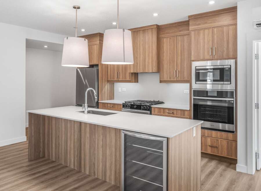 This modern kitchen boasts sleek wood cabinetry, a spacious island with a built-in wine cooler, and stainless steel appliances.