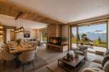 Experience luxury mountain living in this stunning alpine retreat, featuring a modern open-plan living space with a striking wood-clad fireplace and a spacious dining area.
