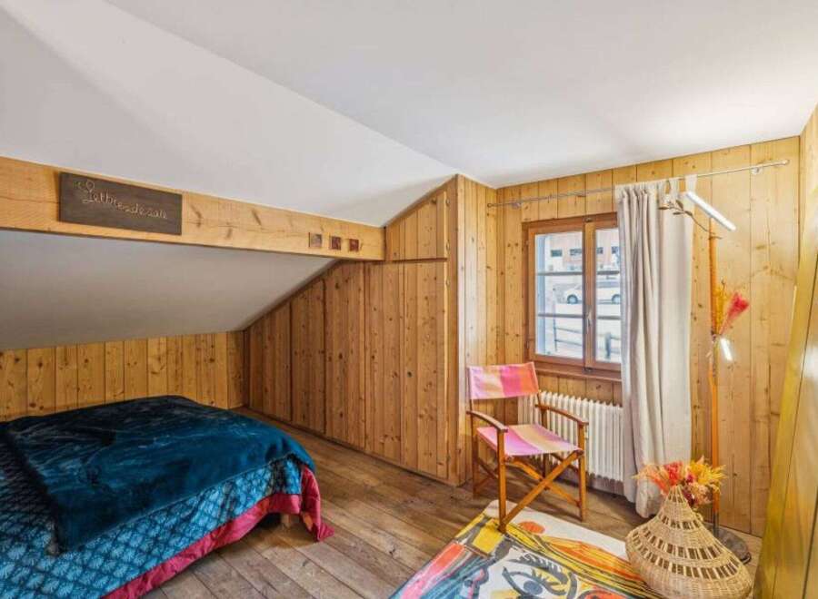 Discover the charm of this cozy bedroom featuring rustic wooden walls and a unique sloped ceiling.