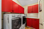 This laundry room features a modern design with vibrant red cabinetry, offering ample storage space.