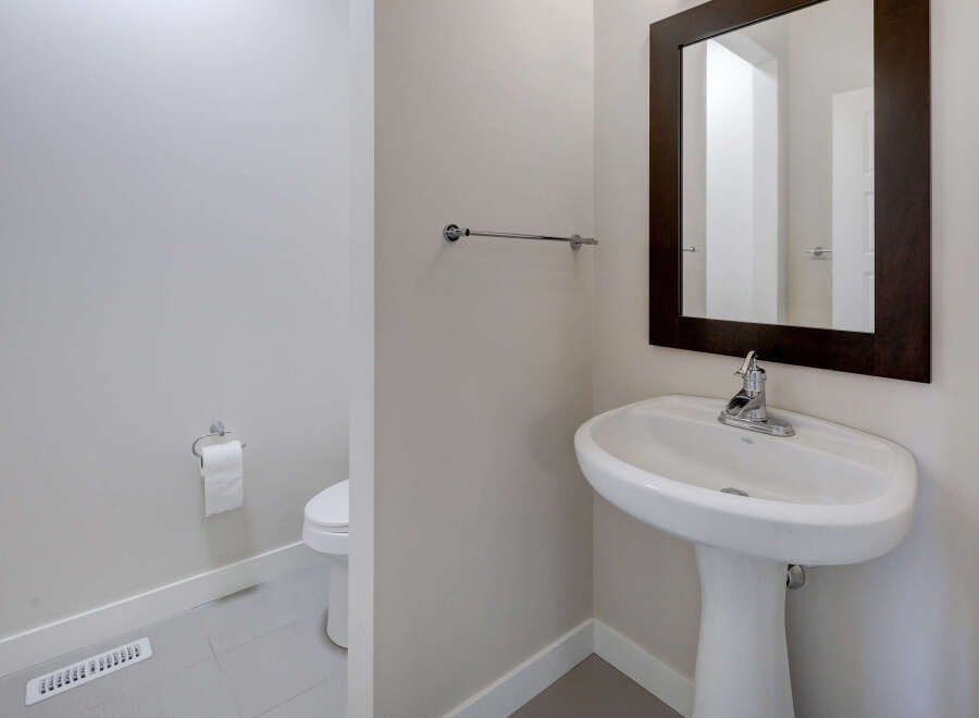 This elegant powder room features a pristine pedestal sink and a stylish dark-framed mirror, creating a sophisticated ambiance.