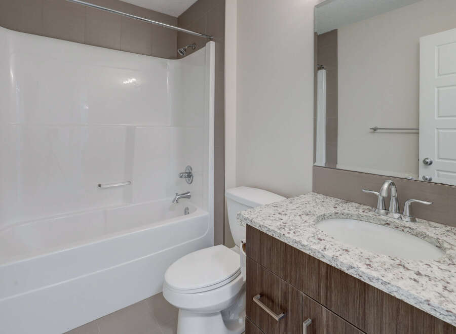 This modern bathroom features a sleek white bathtub and a stylish vanity with a granite countertop.