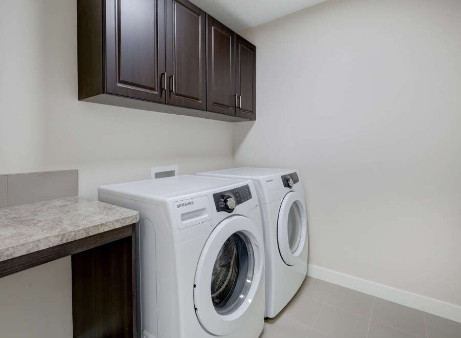 This laundry room features a modern design with sleek white appliances and dark wood cabinetry.