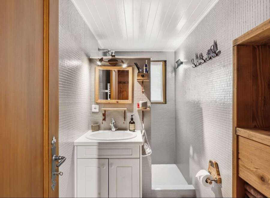 Step into this charming bathroom, featuring a unique design with mosaic tile walls and a wooden vanity.