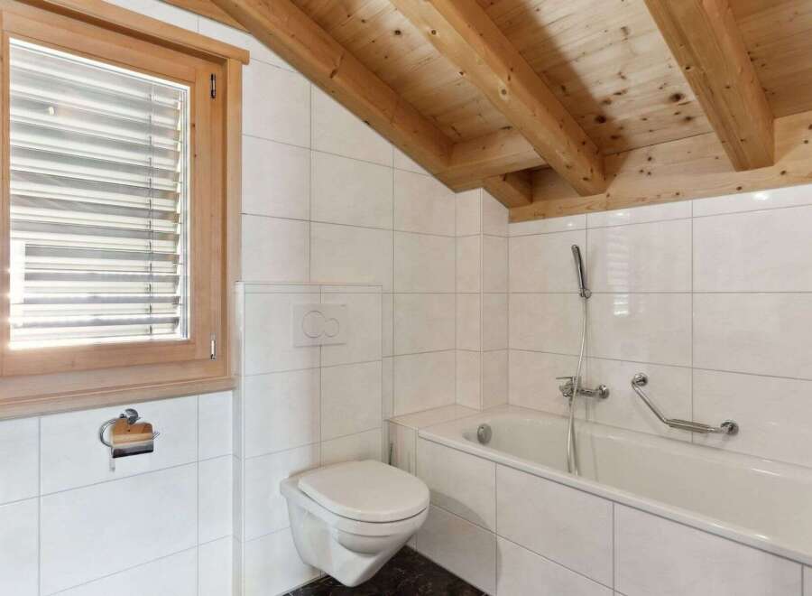 This charming bathroom features a bright and airy design with white tiled walls and a wooden beamed ceiling.