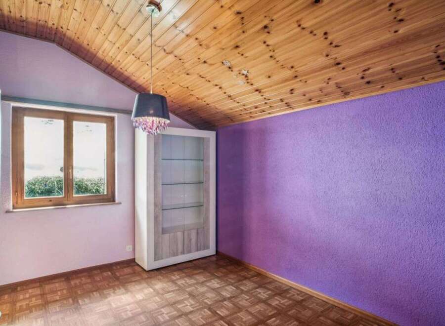 This charming room features a unique wooden ceiling and a vibrant purple accent wall, creating a cozy and inviting atmosphere.