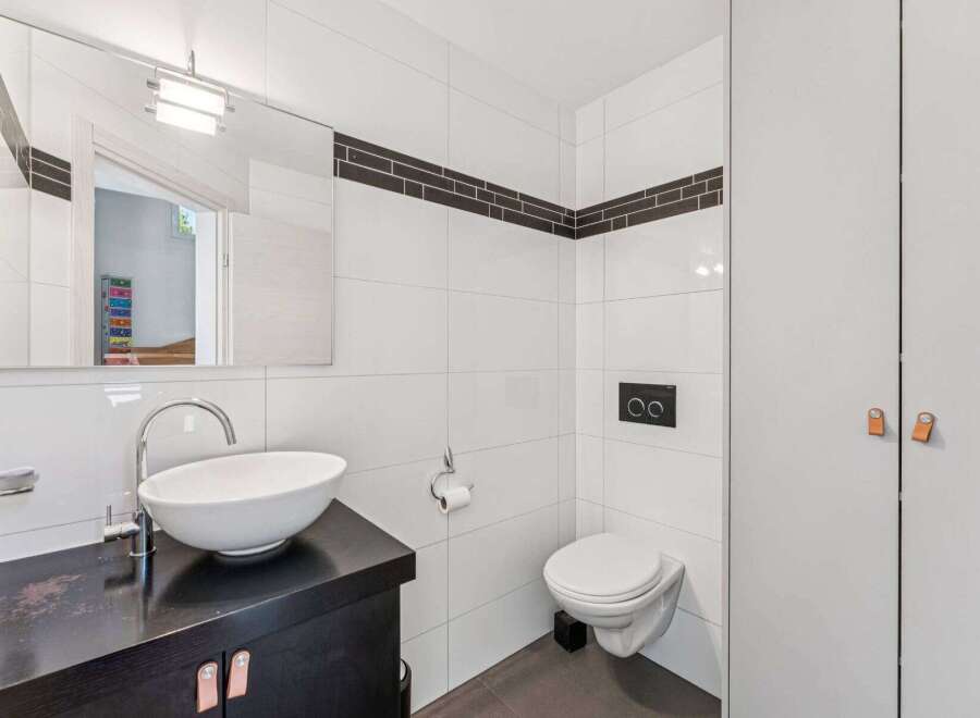 This modern bathroom features sleek white tiles and a stylish black vanity.