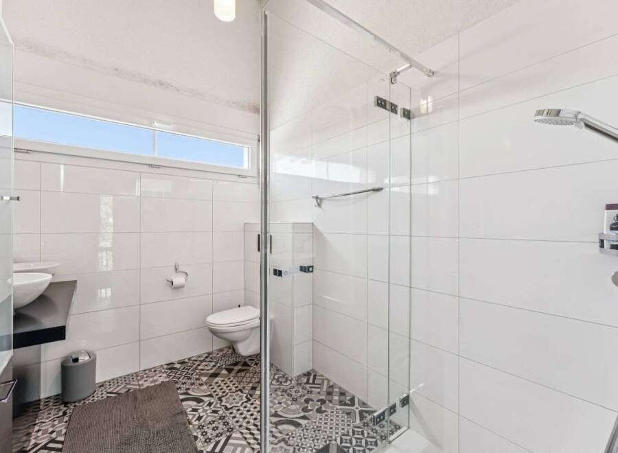 Step into a modern bathroom oasis! This space boasts sleek white tiles, a glass-enclosed shower, and stylish patterned flooring.