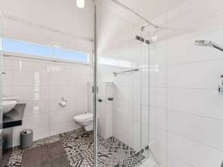 Step into a modern bathroom oasis! This space boasts sleek white tiles, a glass-enclosed shower, and stylish patterned flooring.