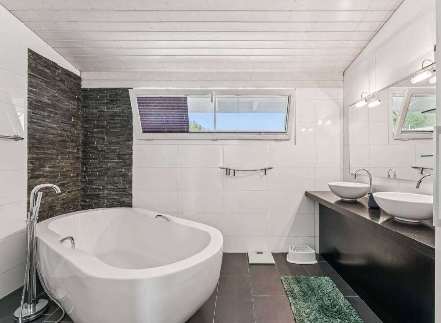 This modern bathroom features a sleek, white bathtub and a stylish stone accent wall, creating a spa-like atmosphere.