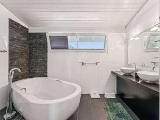 This modern bathroom features a sleek, white bathtub and a stylish stone accent wall, creating a spa-like atmosphere.