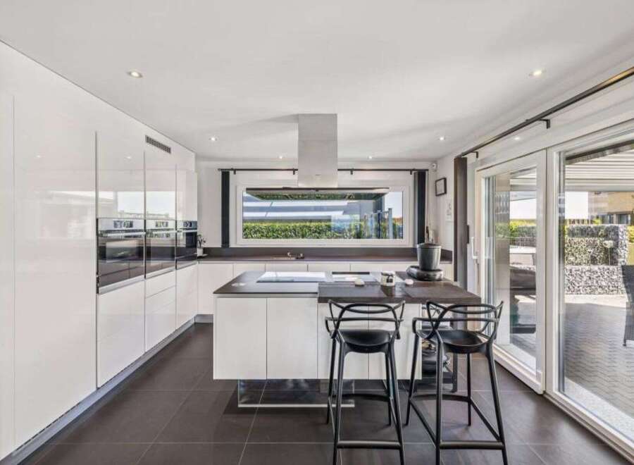 This modern kitchen boasts sleek, white cabinetry and a spacious island, perfect for culinary enthusiasts.