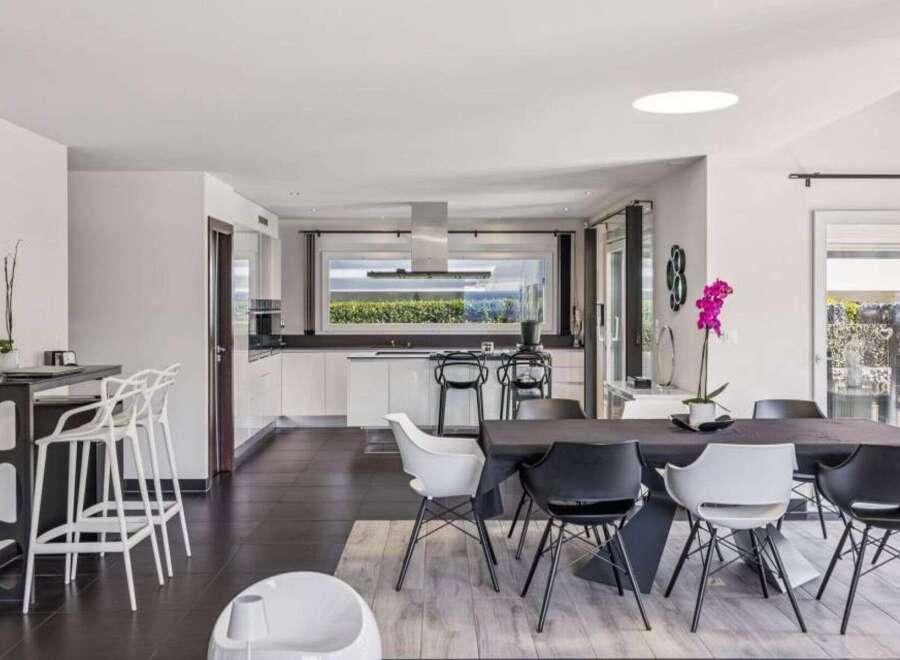 This stunning modern kitchen and dining area boasts sleek white cabinetry, a large island, and a dining table with stylish chairs.