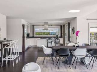 This stunning modern kitchen and dining area boasts sleek white cabinetry, a large island, and a dining table with stylish chairs.