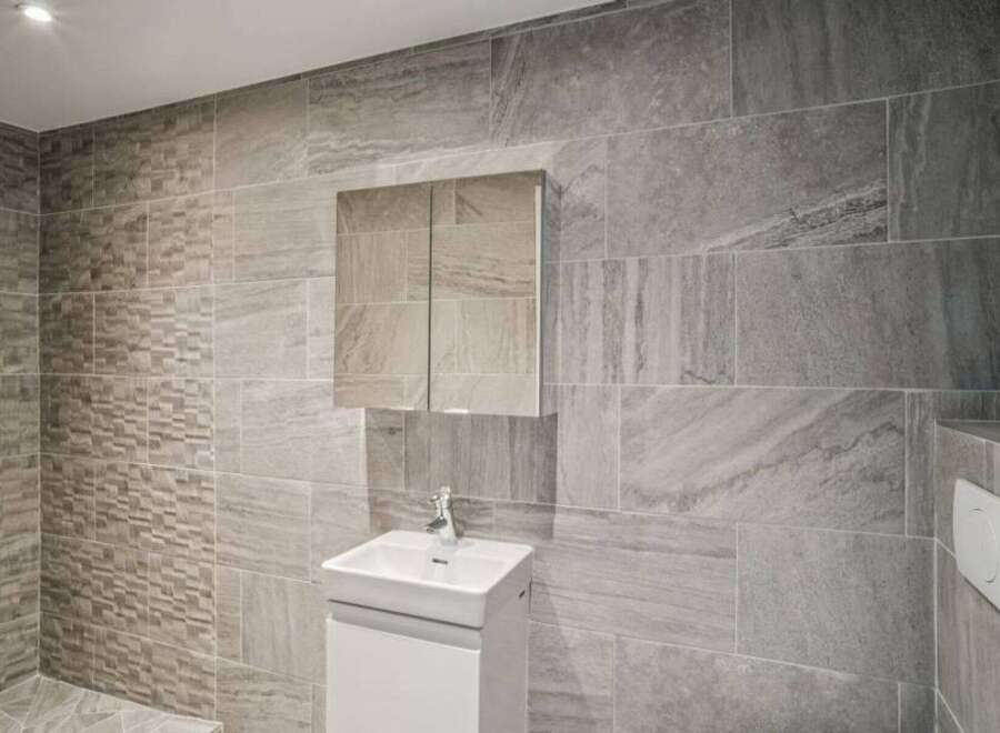 This modern bathroom showcases a sleek design with its gray tiled walls and a minimalist white vanity.