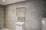 This modern bathroom showcases a sleek design with its gray tiled walls and a minimalist white vanity.