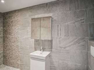 This modern bathroom showcases a sleek design with its gray tiled walls and a minimalist white vanity.
