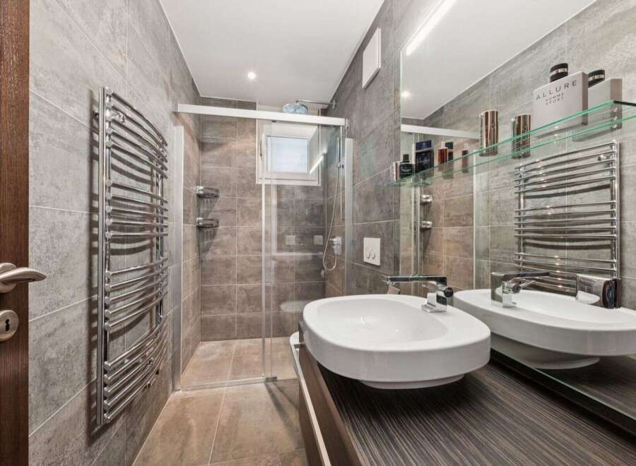 This modern bathroom features a sleek design with gray tiled walls and a glass shower enclosure.