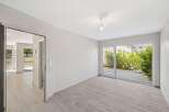Discover modern living in this bright and airy space, featuring sleek light wood-look flooring and expansive glass doors that open to a lush green courtyard.