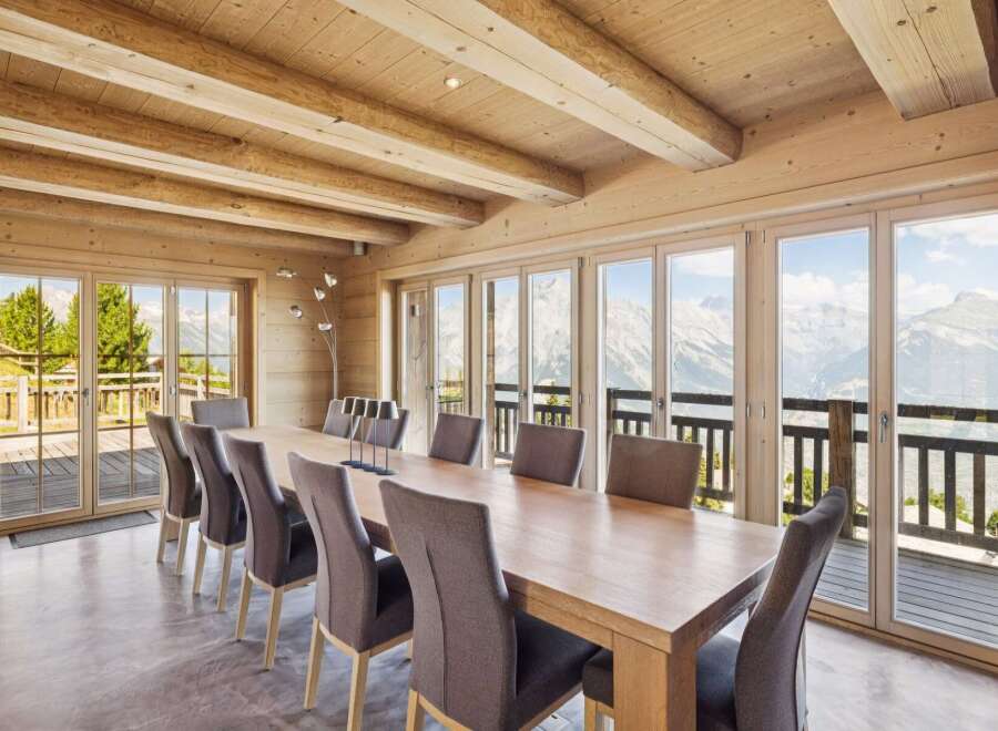 Experience breathtaking mountain views from this stunning dining room, featuring a large wooden table and comfortable upholstered chairs.
