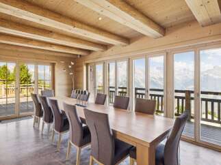 Experience breathtaking mountain views from this stunning dining room, featuring a large wooden table and comfortable upholstered chairs.