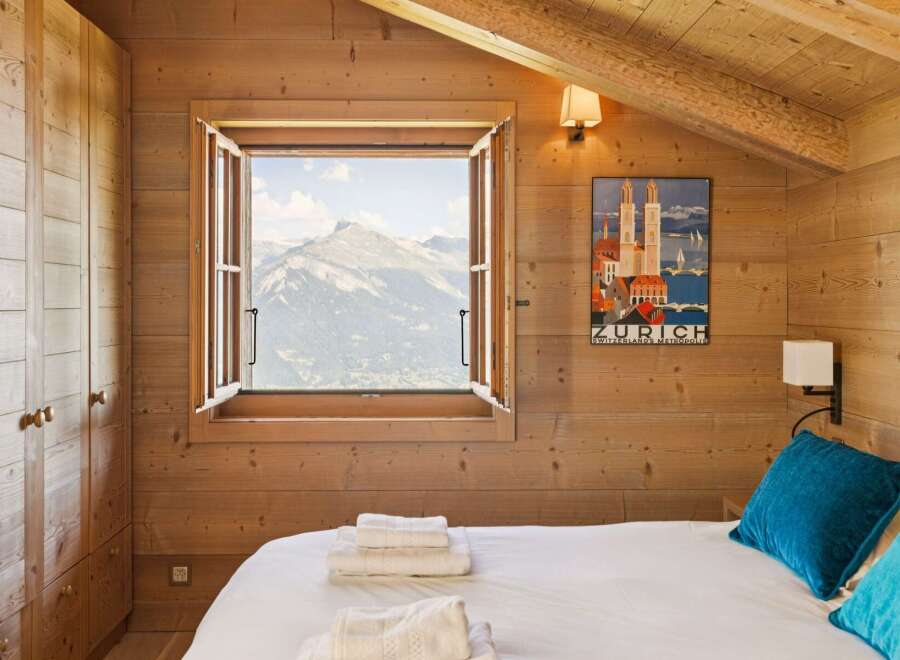 Experience breathtaking mountain views from this charming alpine bedroom, featuring a cozy bed adorned with plush pillows and neatly folded towels.