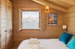 Experience breathtaking mountain views from this charming alpine bedroom, featuring a cozy bed adorned with plush pillows and neatly folded towels.
