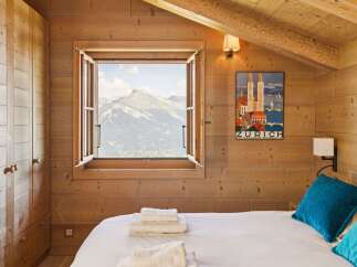 Experience breathtaking mountain views from this charming alpine bedroom, featuring a cozy bed adorned with plush pillows and neatly folded towels.