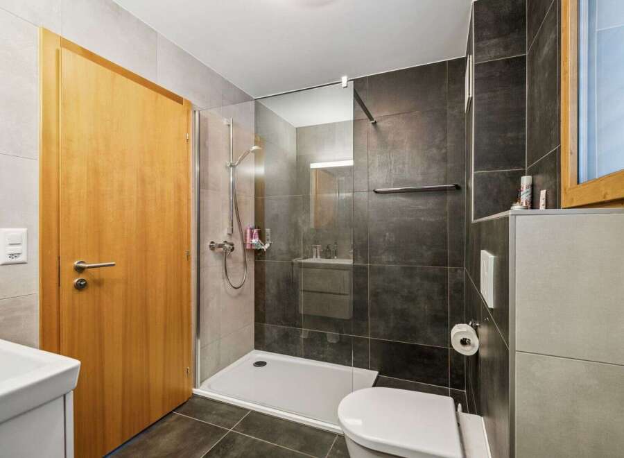 Step into this modern bathroom, featuring a sleek glass-enclosed shower and stylish dark tile accents.