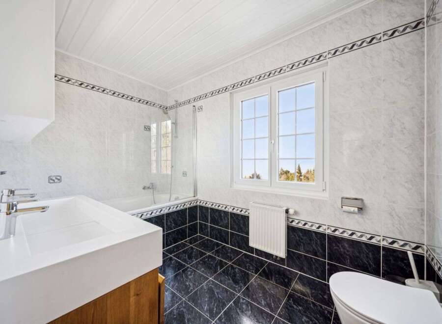 This stunning bathroom features a modern design with sleek white tiles and a contrasting black tiled floor.