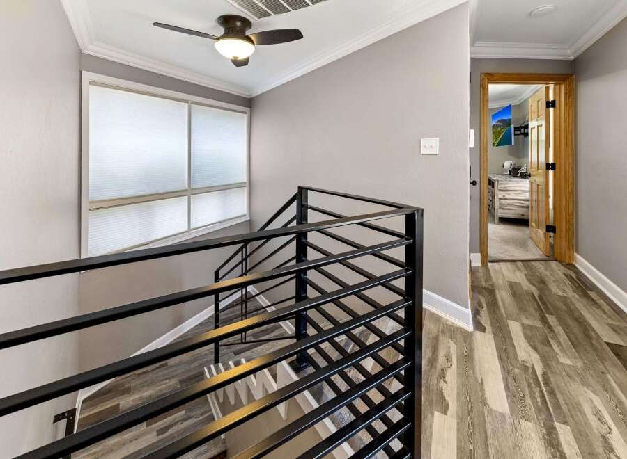 This stunning property features a modern staircase with sleek black railings, leading to a hallway with beautiful wood-look flooring.