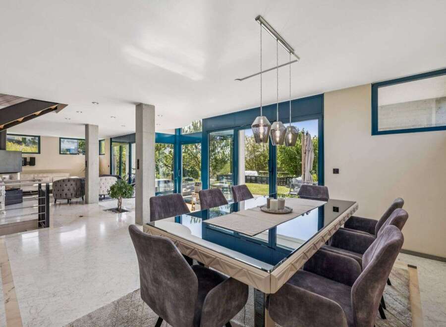Experience luxury living in this stunning property, featuring a modern dining area with a sleek glass table and comfortable seating.