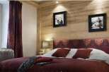 This cozy bedroom features a rustic wooden wall and a comfortable bed with a patterned headboard.