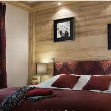 This cozy bedroom features a rustic wooden wall and a comfortable bed with a patterned headboard.