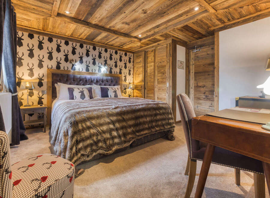 Experience rustic charm in this beautifully appointed bedroom, featuring a luxurious king-size bed with a plush fur throw and a striking deer-themed wallpaper.