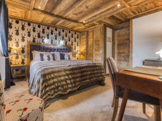 Experience rustic charm in this beautifully appointed bedroom, featuring a luxurious king-size bed with a plush fur throw and a striking deer-themed wallpaper.